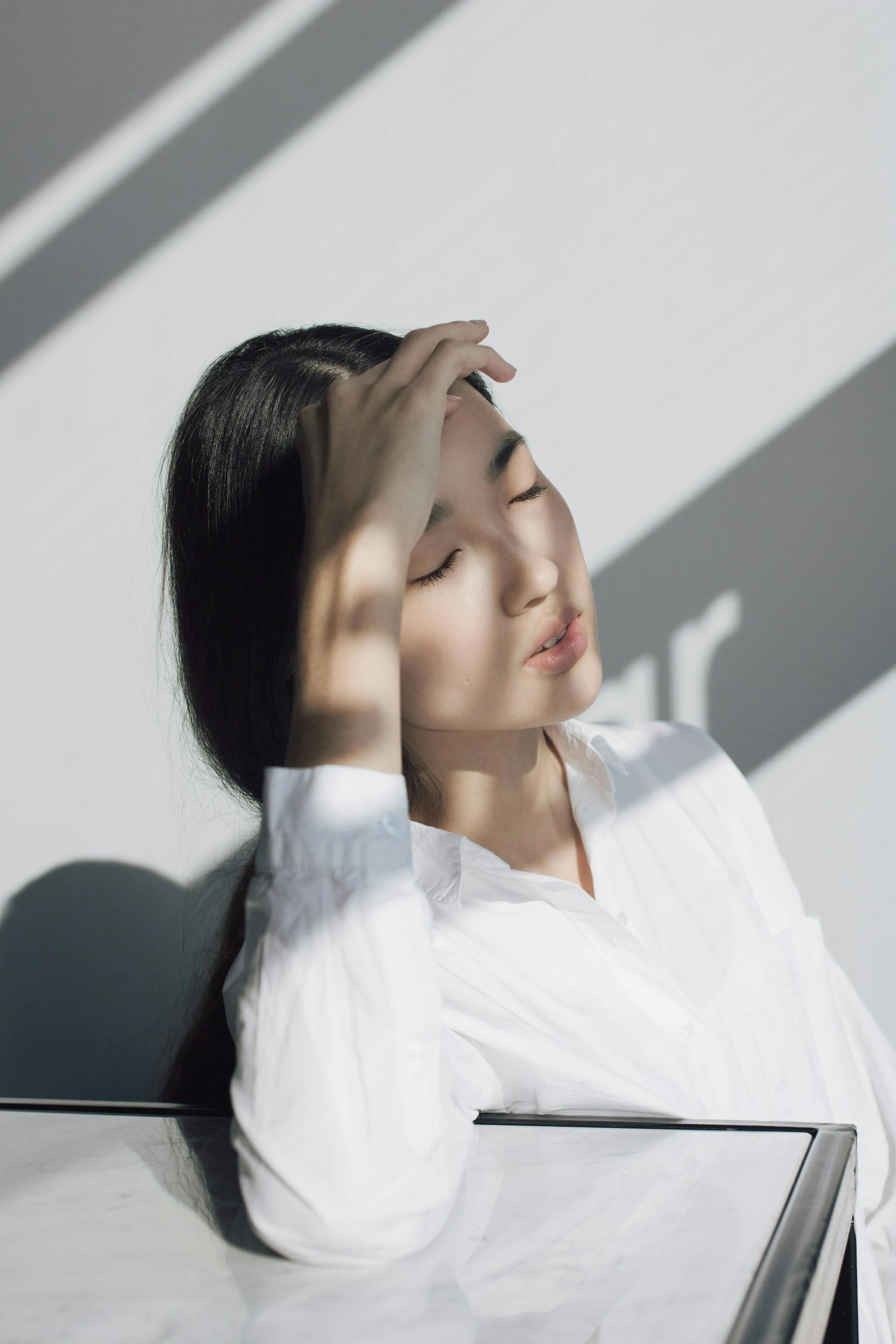 woman-in-white-shirt-with-hand-on-forehead-sunlight-casting-shadows-on-her-face