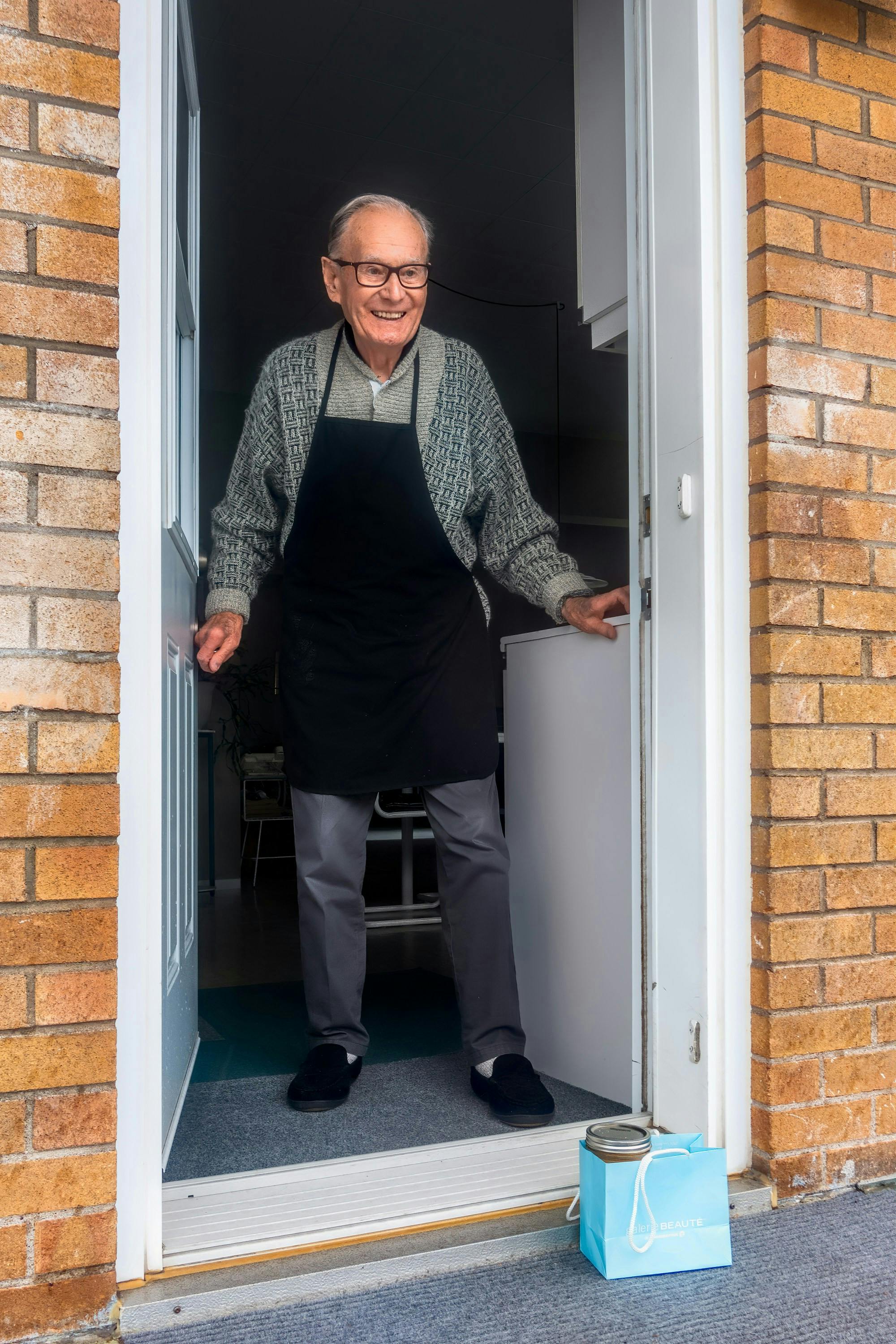 elderly-man-smiling-at-the-doorway-with-a-delivery-bag-outside-his-house